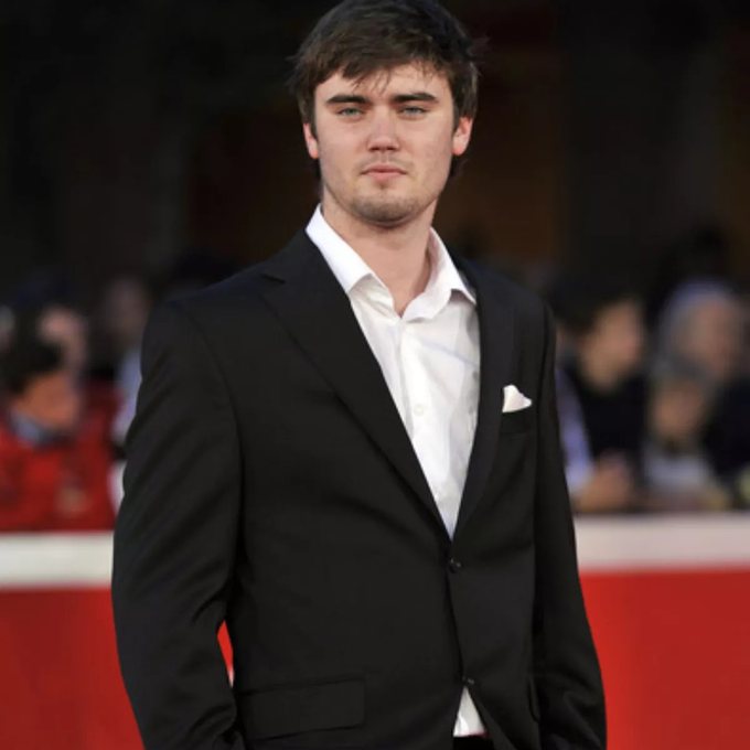 Cameron Bright in a dark suit and white shirt on a red carpet